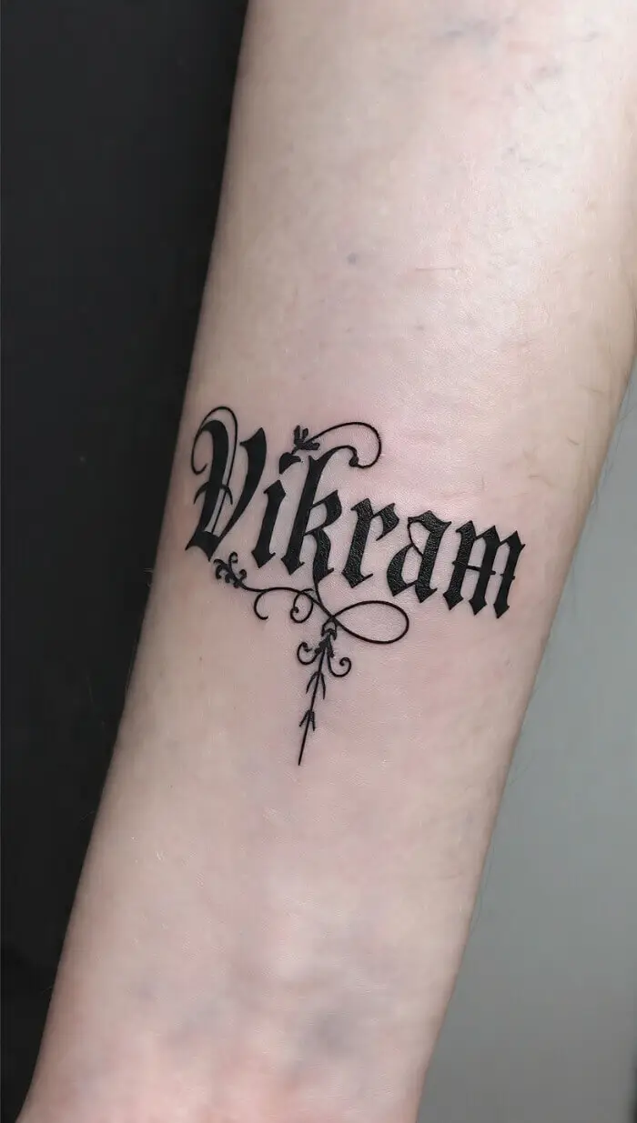"Vikram" Gothic Name Tattoo on Forearm – Elegant Black Ink Script Design